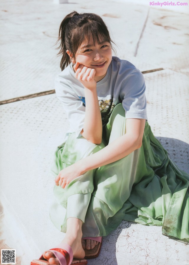 A woman sitting on the ground with her hand on her chin.