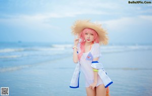 A woman with pink hair wearing a straw hat on the beach.