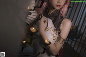 A woman with pink hair sitting on a bed.