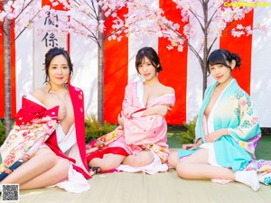 A woman in a pink kimono standing in front of a cherry blossom tree.