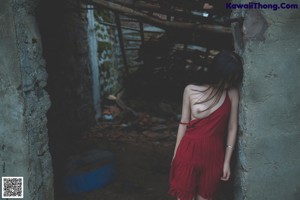 A naked woman in a red dress standing in front of a stone wall.