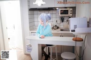 A woman with blue hair is sitting on a bed.