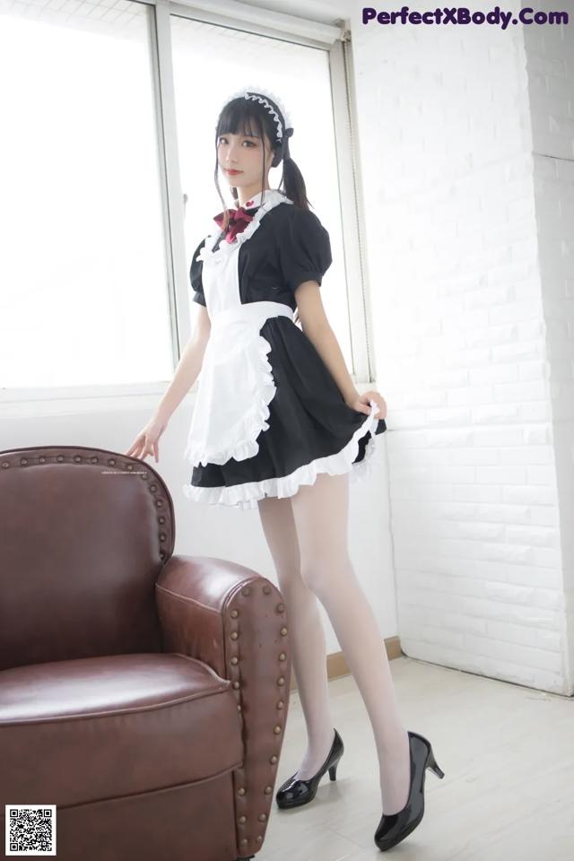 A woman in a maid outfit standing next to a brown chair.