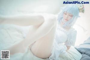 A woman in a white dress sitting on a bed.