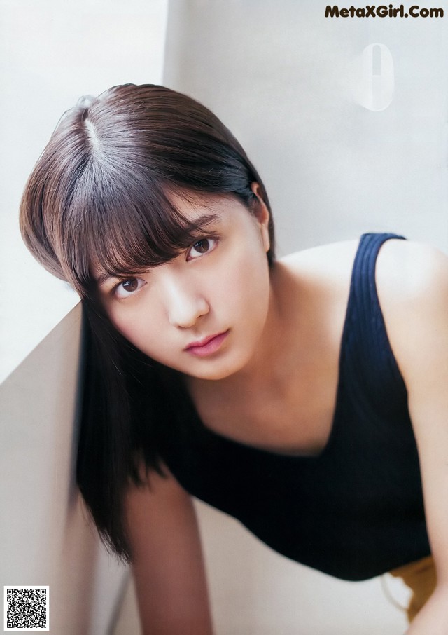 A woman in a black tank top leaning against a wall.