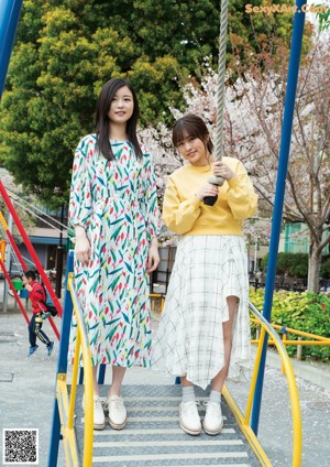 Two young women sitting on the ground in front of a tree.