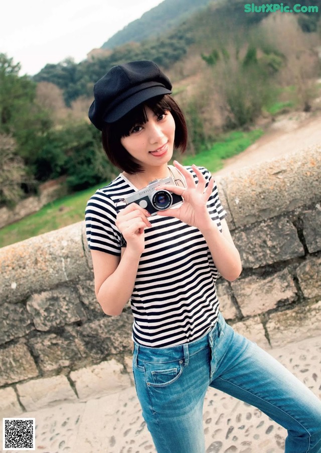 A woman in a striped shirt and hat holding a camera.