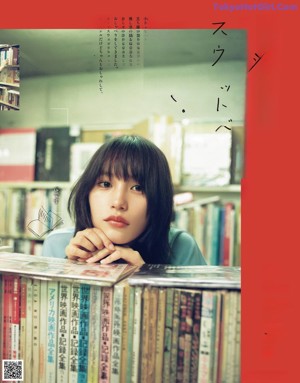 A woman leaning on a stack of books in a library.