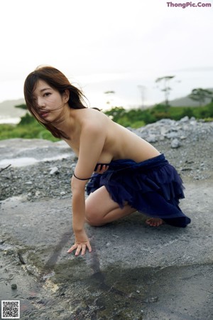 A naked woman leaning against a wall with a towel around her neck.