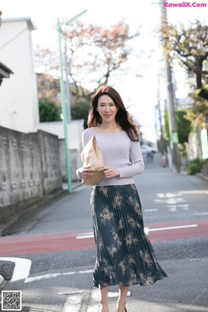 A woman walking down a sidewalk holding a purse.