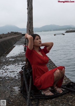 A woman in a red dress sitting on a rock.