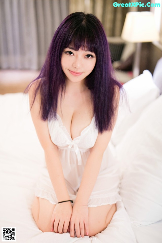 A woman with purple hair sitting on a bed.