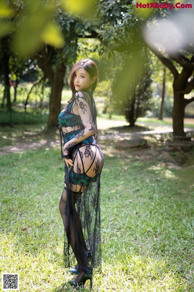 A woman in a black and green lingerie posing in the grass.