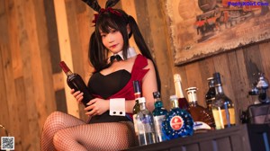 A woman in a bunny costume crouching down next to a bottle of champagne.
