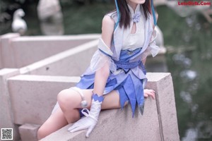 A woman in a blue dress standing on a rock by a pond.