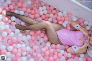 A woman in a pink bunny costume sitting in a bathtub filled with pink and white balloons.