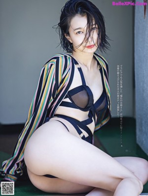 A woman in a black bikini sitting on the ground.