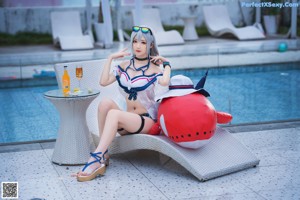 A woman in a bikini and hat sitting by a pool.