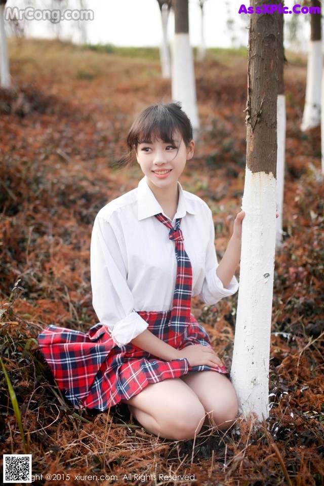 A woman in a school uniform sitting next to a tree.