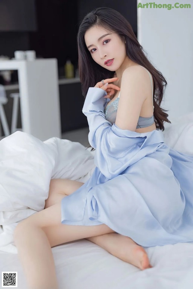 A woman in a blue dress sitting on a bed.