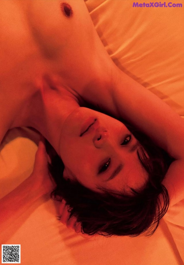 A naked woman laying on a bed with her eyes closed.