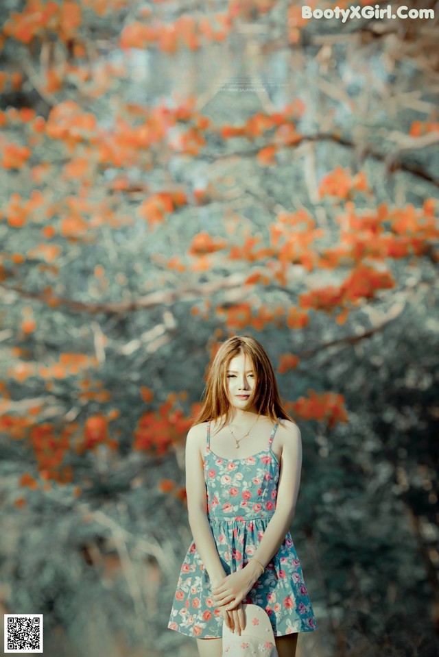 A woman in a blue dress standing in front of a tree.