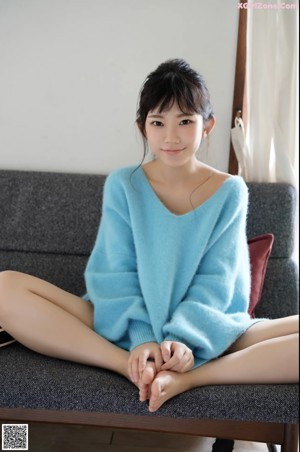A woman in a blue sweater sitting next to a potted plant.