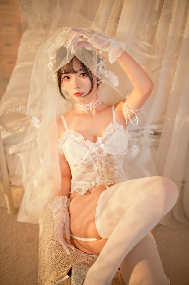 A woman in a white lingerie sitting on a bed.