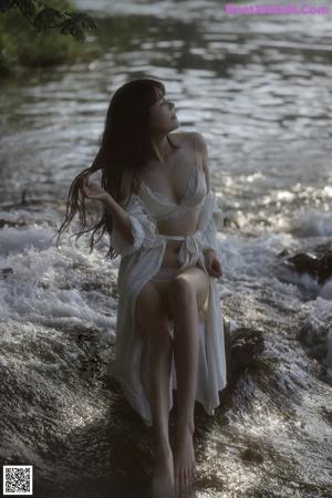 A woman in a white dress standing in a stream.