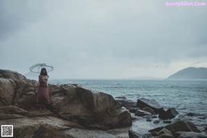 A naked woman standing on a rock by the ocean.