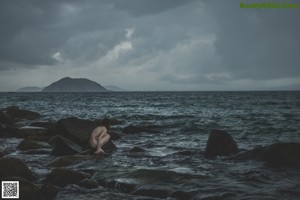 A woman sitting on a concrete wall by the ocean.