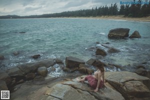 A woman sitting on a rock holding an umbrella.