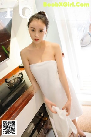 A woman in a white towel leaning against a washing machine.