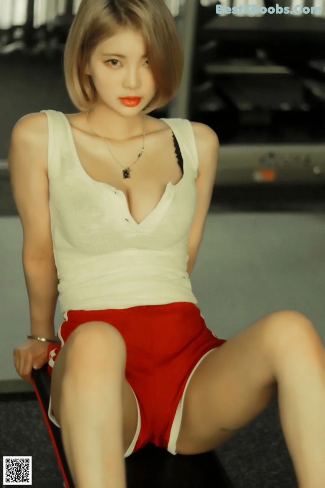 A woman in a white tank top and red shorts sitting on a bench.