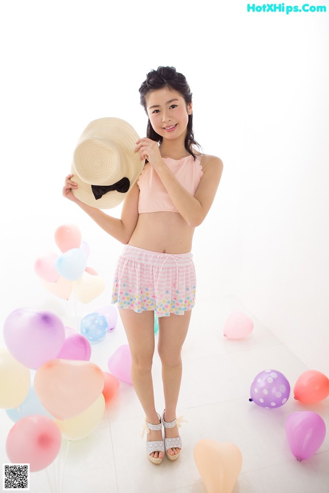A young woman holding a straw hat in front of balloons.