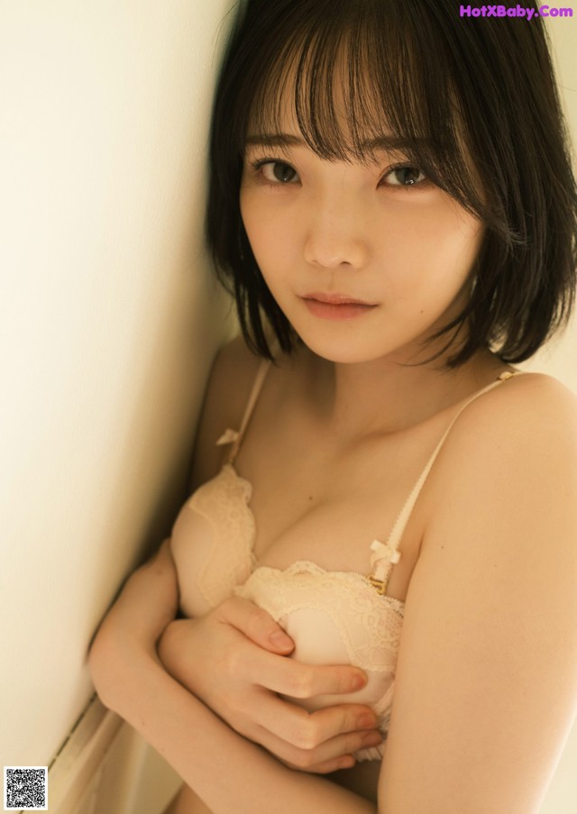 A woman in a white bra and panties leaning against a wall.