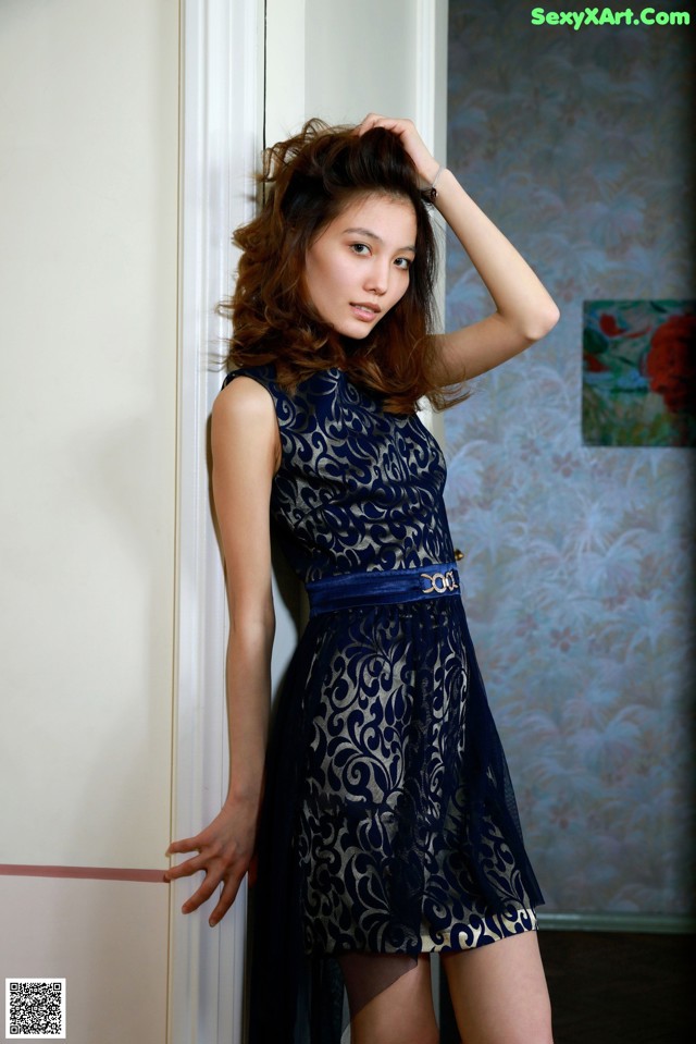 A woman in a blue dress leaning against a wall.