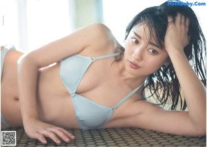 A woman in a pink bikini sitting on a bed.