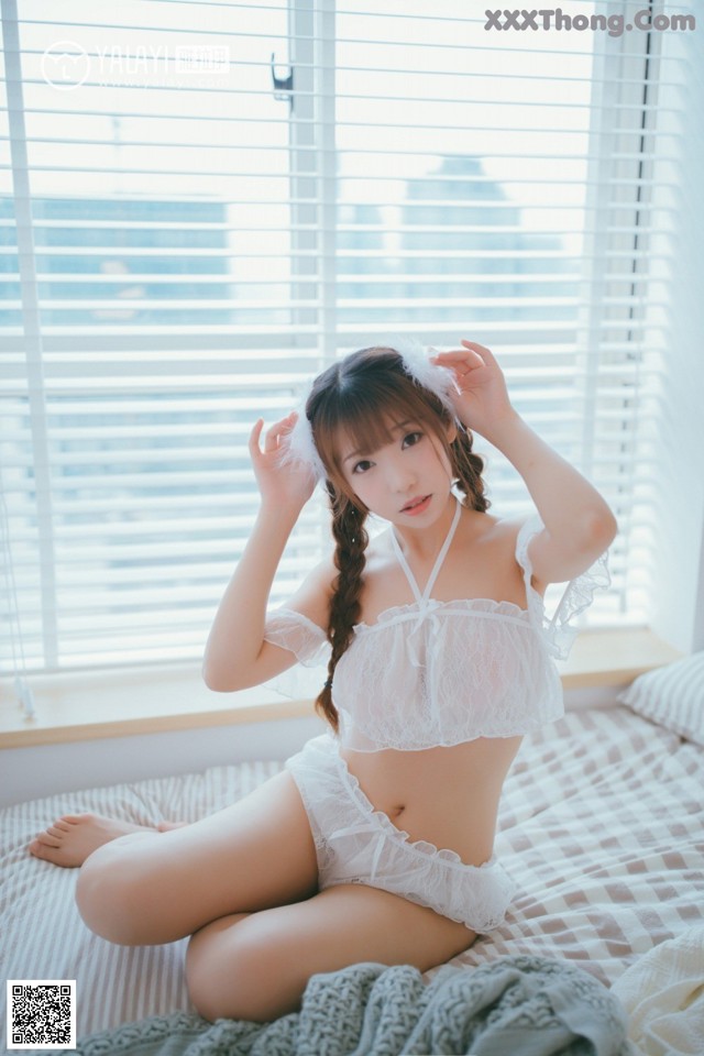 A woman in a white lingerie sitting on a bed.