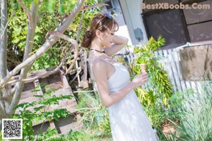 A woman in a white dress standing in front of a bush.