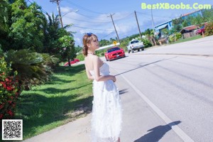 A woman in a white dress standing on the side of a road.