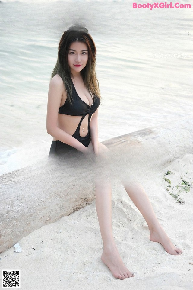 A woman in a black bathing suit sitting on a rock by the water.