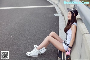 A woman in a white dress holding a skateboard on a road.